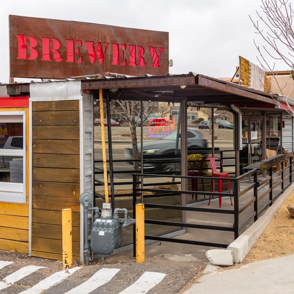 The 377 Brewery's exterior, featuring a rustic "BREWERY" sign and an outdoor patio with red chairs.