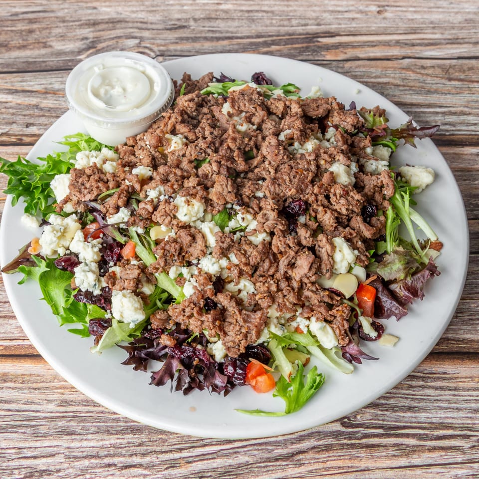 A large salad with ground meat, crumbled cheese, and mixed greens, served with a side of dressing.
