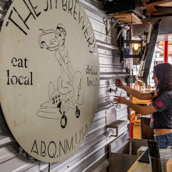 A bartender fills a glass with water next to a large circular sign for The 377 Brewery.