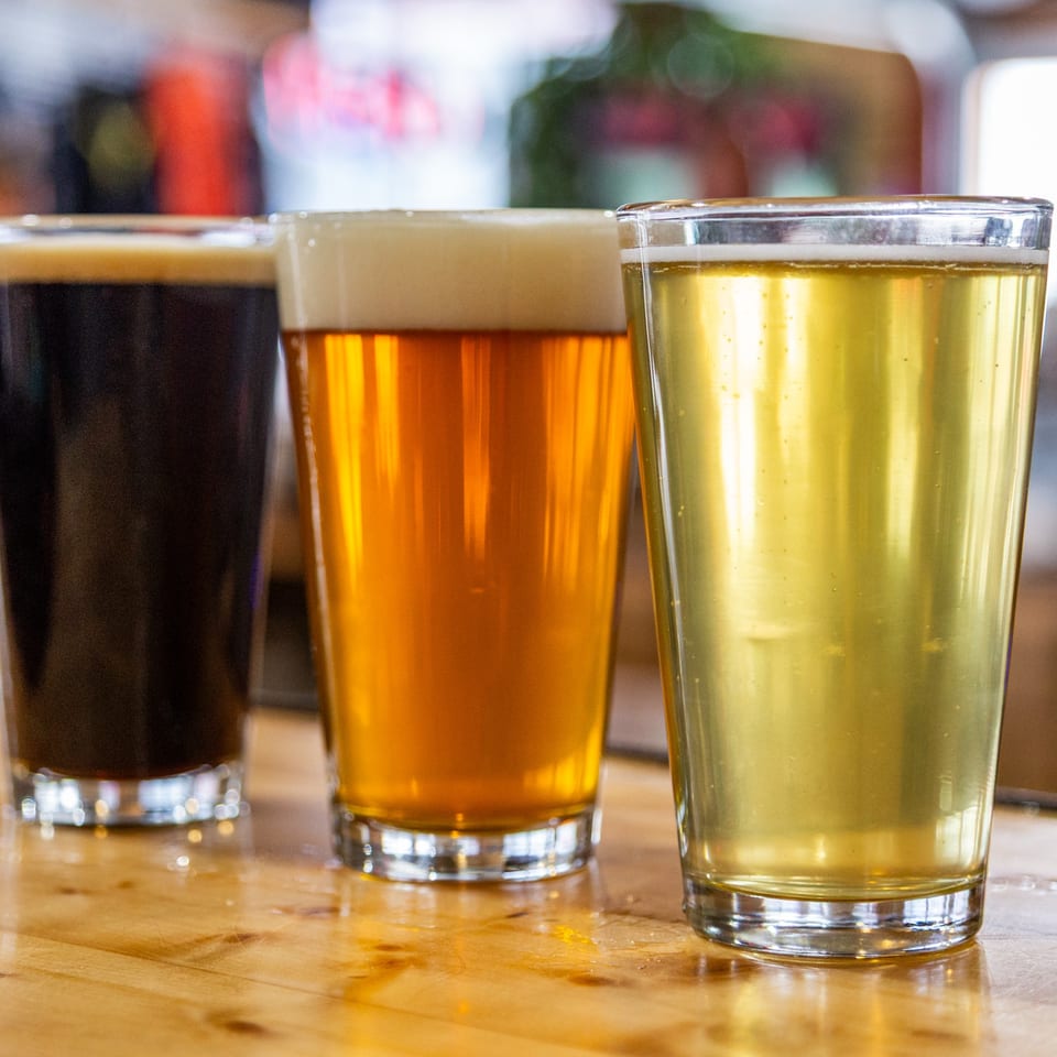 Three glasses of beer, dark, amber, and pale, on a wooden bar top at The 377 Brewery.