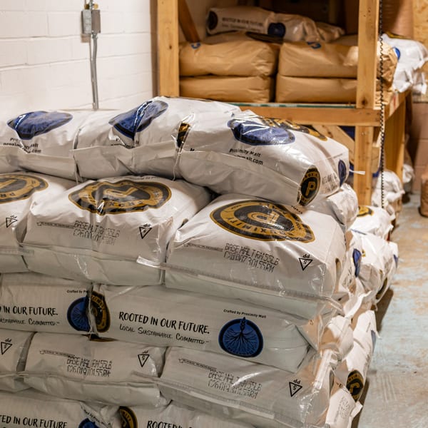Stacked bags of "Proximity Malt" in a brewery storage area, ready for brewing.