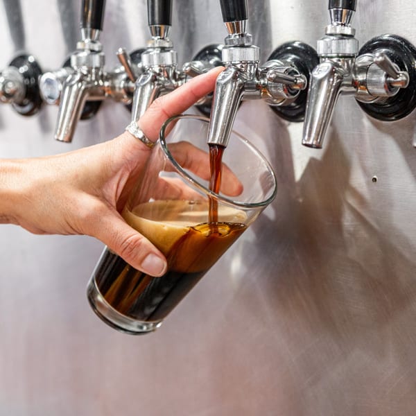 A hand holding a glass under a tap, pouring dark beer at The 377 Brewery.
