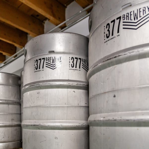 Several silver beer kegs with "The 377 Brewery Albuquerque, NM" logo are stacked in a storage area.