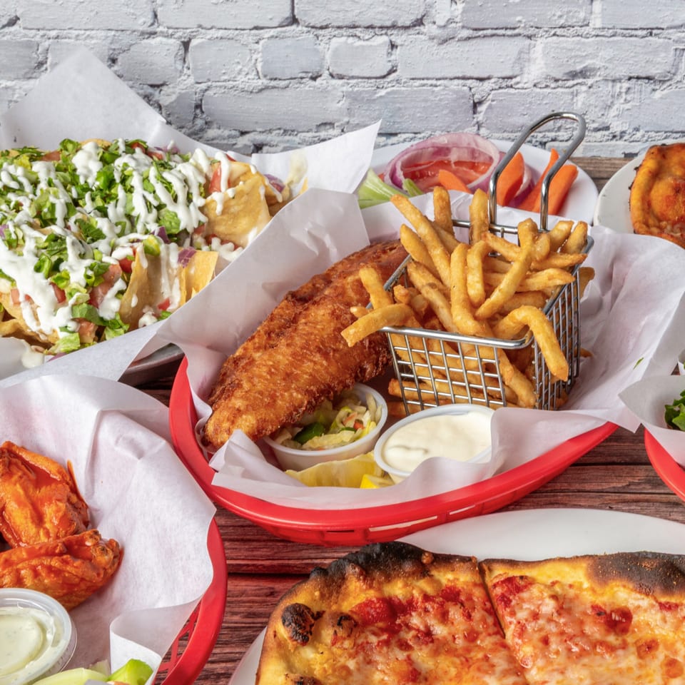 A table laden with nachos, fish and chips, buffalo wings, and a cheese pizza from The 377 Brewery.