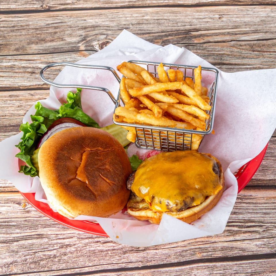 Cheeseburger with lettuce, onion, and pickles, served with a side of fries in a metal basket.
