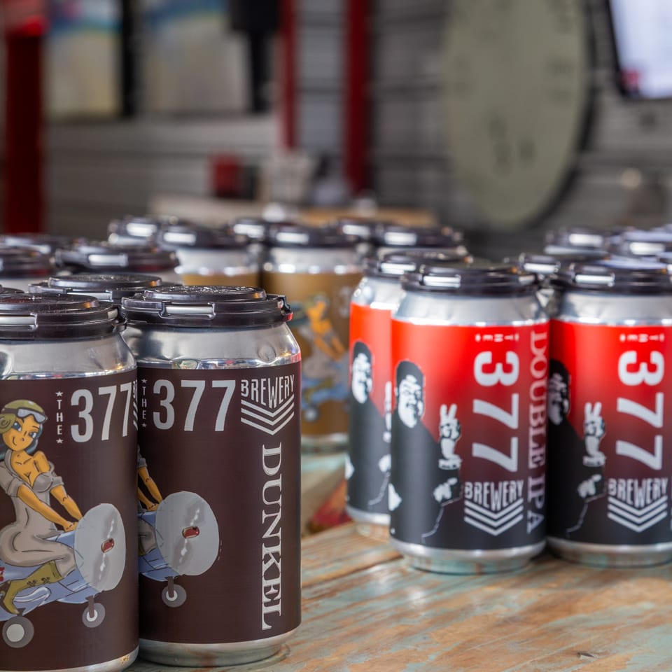 Rows of 377 Brewery beer cans, including Dunkel and Double IPA, on a wooden surface.