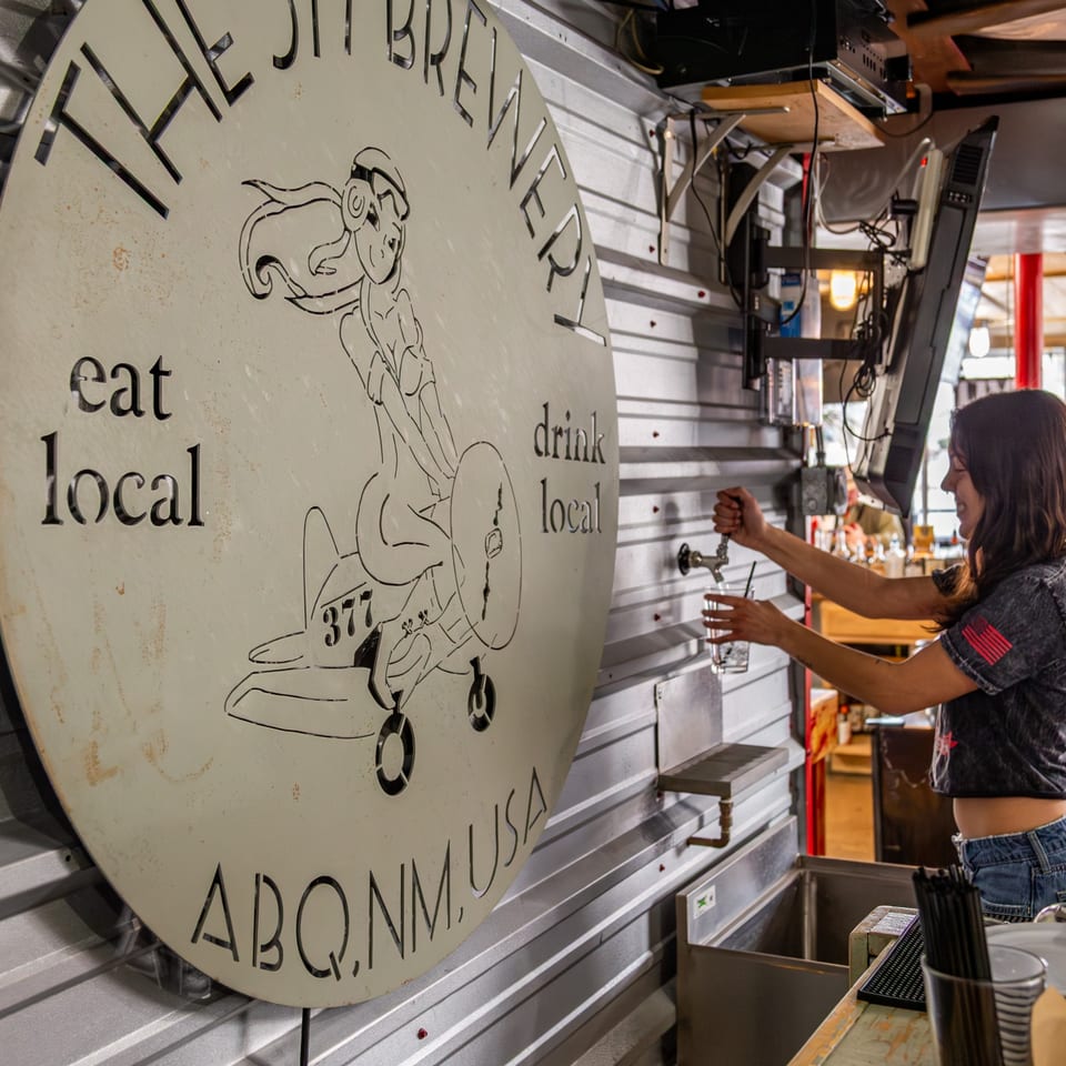 A bartender fills a glass with water next to The 377 Brewery's circular logo sign.
